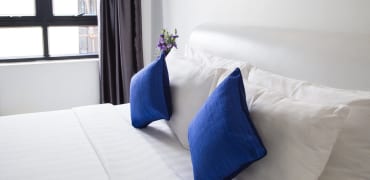Bed in white linen with two blue throw pillow as accent