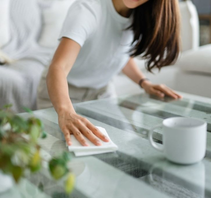 woman dusting and wiping down the surface of a coffee table