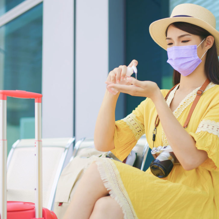 female traveler wearing mask and using sanitizer to disinfect her hands