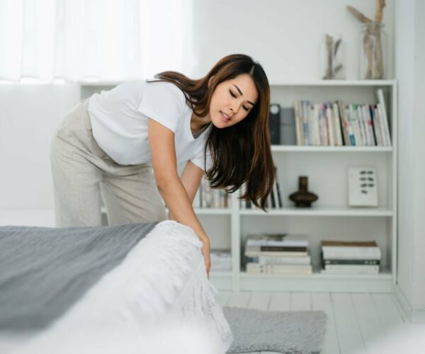 Young woman arranging pillows and making up bed at home