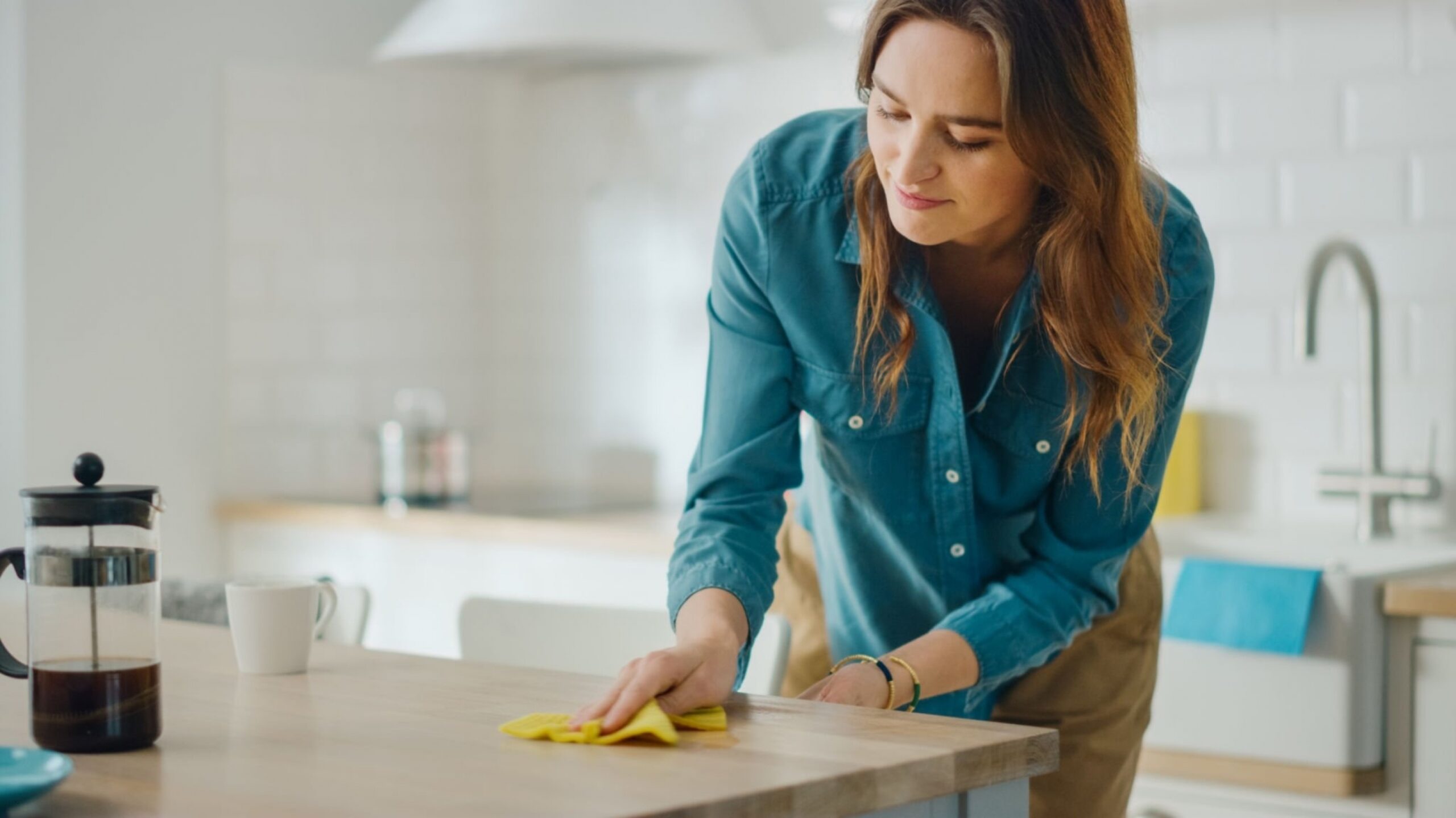 Caring Housewife Wiping Spilled Coffee or Crumbs from a Wooden Kitchen Table.